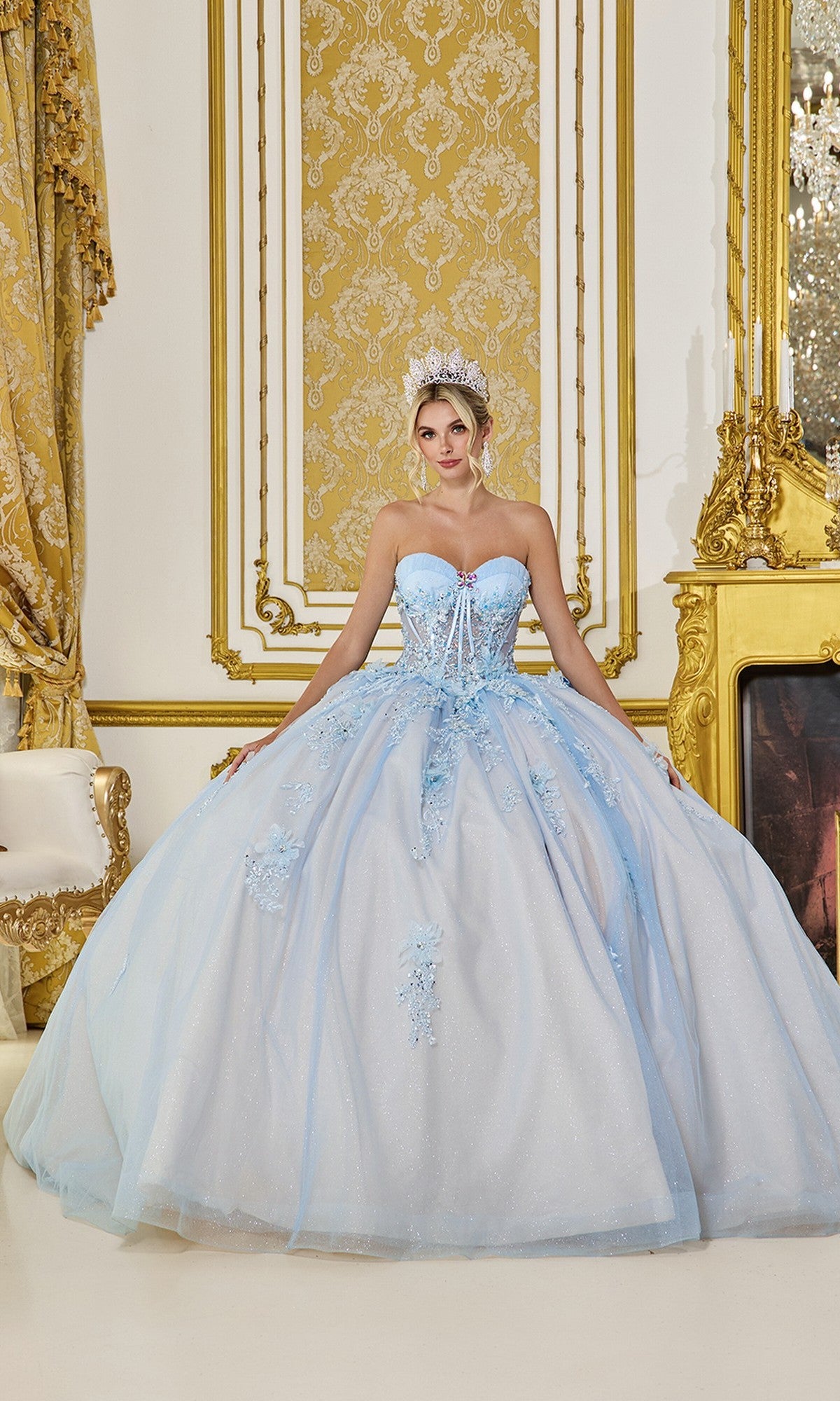 A woman in the Quinceanera Dress 5058 By Dancing Queen, featuring 3D flowers and a sweetheart corset in Bahama Blue, stands in a gold-accented ornate room, her tiara adding to the fairytale-inspired look.